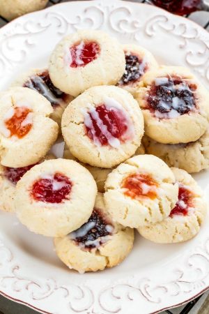 Thumbprint Cookies - an easy 5 ingredient dough to make 7 different Christmas cookies including raspberry, apricot and strawberry jam filling, Hershey's Kisses, Nutella and white chocolate with crushed peppermint candy canes! Best of all there's NO spreading or CHILLING required! Perfect for your holiday cookie platter!